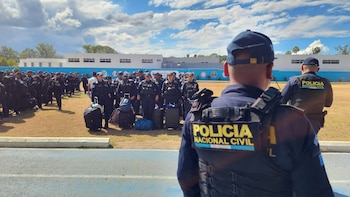Agentes de la Policía Nacional Civil de Guatemala en uniformes oscuros y chalecos, con equipaje, reunidos al aire libre en un campo bajo un cielo nublado