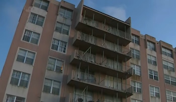 Vista en ángulo bajo de un edificio residencial de color salmón con múltiples pisos, ventanas rectangulares y balcones con barandales metálicos