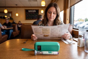 Una mujer lee la carta en la mesa de un restaurante donde yacen un estuche verde y un inyector de Zepbound