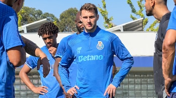 Un jugador de fútbol vestido con camiseta azul de manga larga del FC Porto está de pie junto a otros compañeros de equipo.