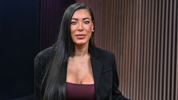 Retrato de medio cuerpo de Lady M, una mujer de cabello oscuro largo y ojos azules, vistiendo un blazer negro sobre un top burdeos, en un estudio