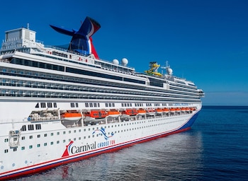 Vista lateral de un gran crucero blanco con franjas rojas y azules, con el nombre 'Carnival Splendor' y botes salvavidas naranjas, navegando en el océano azul