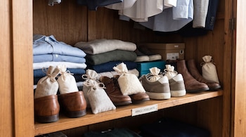 Estante de madera con ropa doblada, varios pares de zapatos con saquitos de tela y una etiqueta con el texto arroz desecante.