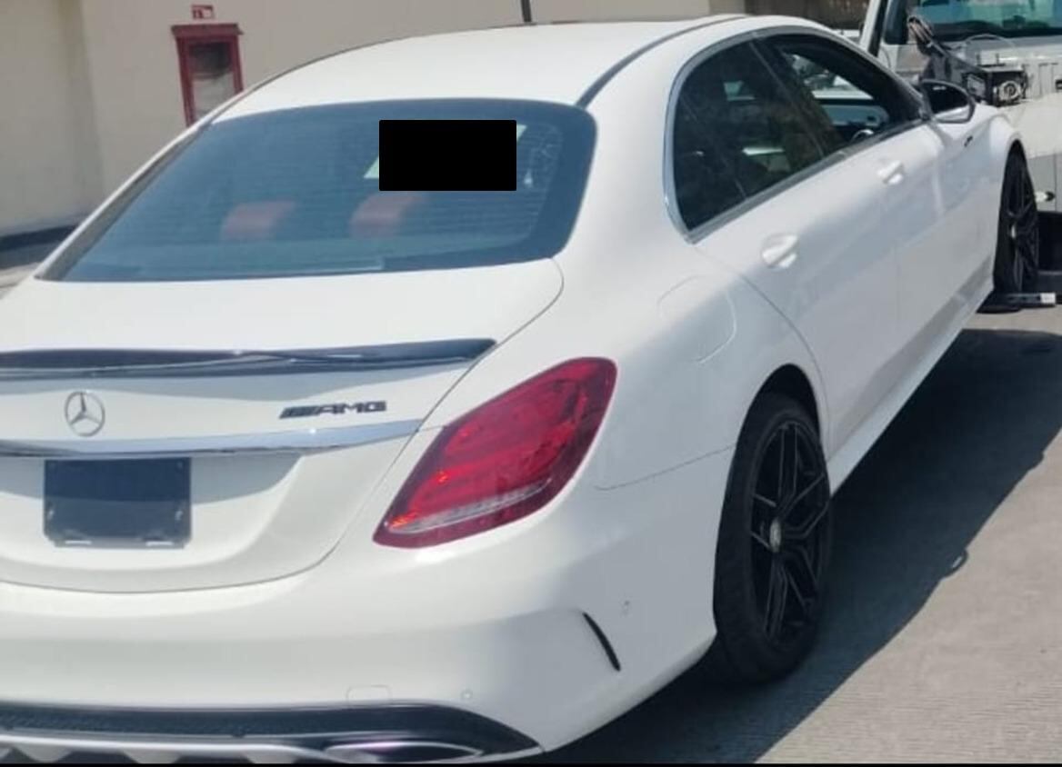 Un lujoso Mercedes-Benz AMG blanco se muestra desde su parte trasera, destacando su diseño deportivo, elegantes rines negros y detalles cromados bajo la luz del sol.