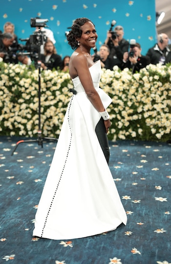 Deborah Roberts vistió un conjunto que combina estructura y contraste: un top blanco sin tirantes de líneas arquitectónicas, que se prolonga hacia una sobrefalda larga y abierta por detrás, confeccionada en el mismo tejido blanco rígido. Esta pieza presenta una hilera vertical de botones negros a lo largo de la espalda y un cinturón negro que marca la cintura