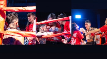 Boxeador tatuado en el ring, acompañado por tres mujeres de su equipo, quienes le ofrecen agua y asisten durante el combate. Ropas naranjas del ring.