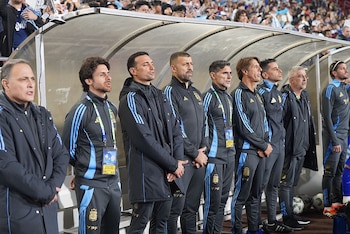 Grupo de hombres, incluyendo Daniel Martínez, con uniformes deportivos negros y celestes, de pie en un banquillo de fútbol. Se ve una multitud al fondo