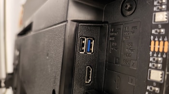 Un puerto USB 3.0 azul, un puerto HDMI, texto con especificaciones eléctricas y parte de una placa de circuito impreso con componentes electrónicos.