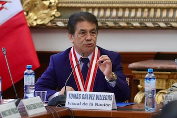 Primer plano del Fiscal de la Nación, Tomás Gálvez Villegas, hablando en una mesa de trabajo con un micrófono, vistiendo un traje azul y una banda bicolor