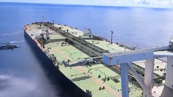 Vista aérea de un gran buque petrolero navegando en mar abierto, con un helicóptero volando bajo a su lado y otro sobre la cubierta