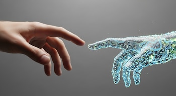 Primer plano de una mano humana extendiéndose hacia una mano transparente formada por circuitos brillantes de color azul y verde sobre un fondo gris liso.