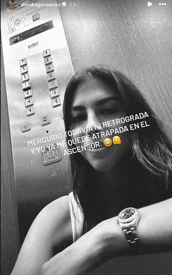Fotografía en blanco y negro de una mujer sentada dentro de un ascensor frente al panel de botones, con un texto sobreimpreso