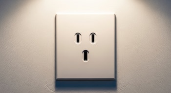 Primer plano de un enchufe eléctrico blanco de tres orificios en una pared blanca texturizada. La iluminación superior crea sombras y un brillo sutil.