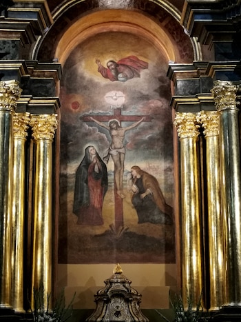 Pintura de Jesucristo crucificado con dos figuras a sus pies y dos columnas doradas a los lados en una hornacina