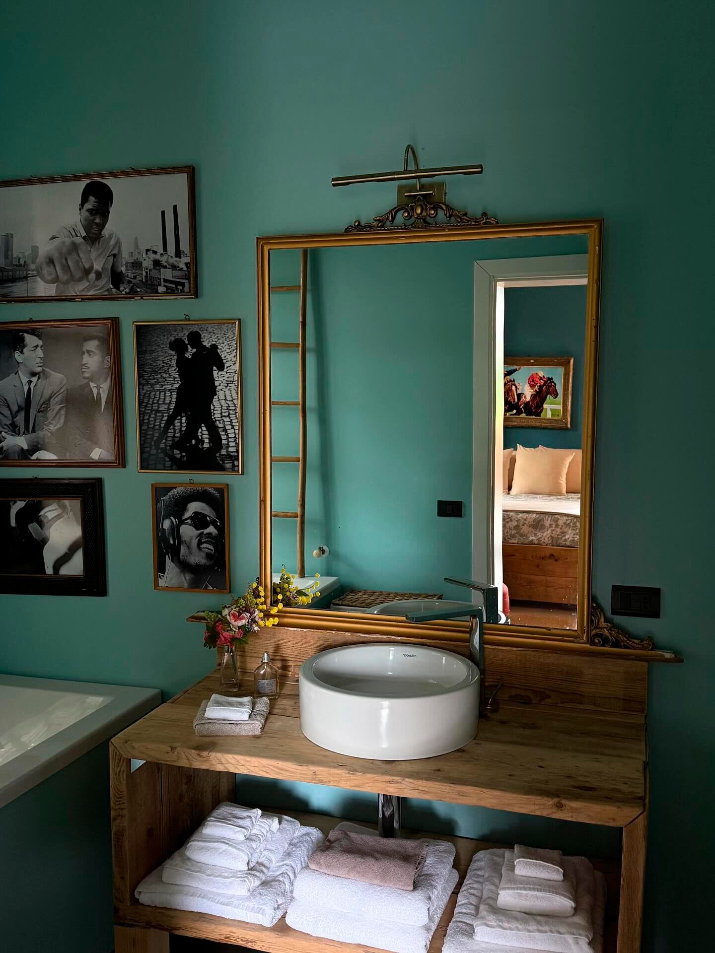 El baño, repleto de cuadros con figuras conocidas, un espejo dorado y flores frescas