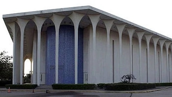Un edificio de concreto con una larga fachada de arcos repetitivos. Algunas secciones tienen paneles verticales de mosaico azul. El edificio tiene un techo plano