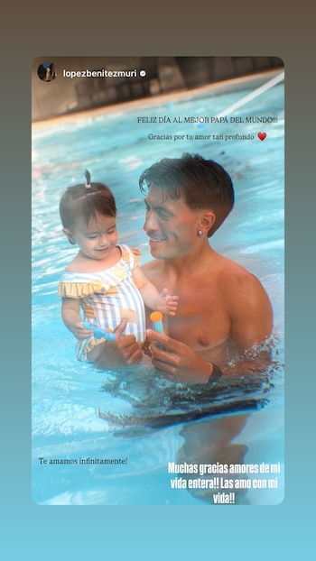Hombre sonriente con torso desnudo y pendiente en la oreja abraza a una niña con traje de baño a rayas mientras están en una piscina