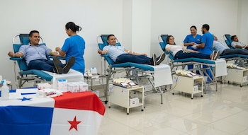 Varias personas recostadas en sillas de donación recibiendo transfusiones, asistidas por personal médico, con una bandera de Panamá en la mesa principal.