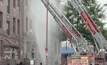 Dos camiones de bomberos con escaleras extendidas hacia un edificio de ladrillo del que sale humo en el Upper West Side de Nueva York