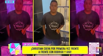 Christian Cueva de pie, mirando al frente, con una camiseta oscura con la palabra "Madre" y pantalones cortos azules, en un set de televisión con luces