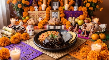 Plato con mole, arroz y tortillas en una mesa con flores de cempasúchil, velas encendidas, papel picado, calaveritas y pan de muerto.