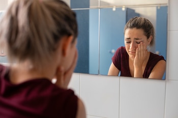 Una mujer se mira triste en el espejo después de un mal episodio