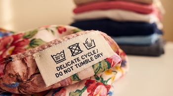 Primer plano de etiqueta de cuidado en prenda floral con símbolos de lavado a 30°C, ciclo delicado y no usar secadora. Texto: DELICATE CYCLE / DO NOT TUMBLE DRY.