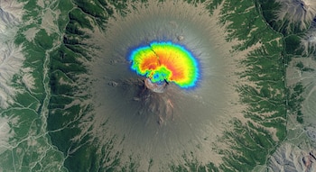 Vista aérea de un volcán con vegetación en los alrededores y terreno árido. Un mapa de calor de colores vivos cubre la cima del cráter principal.