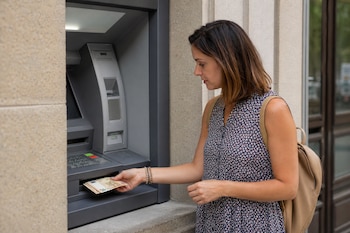 Una mujer toma varios billetes de cincuenta euros de la ranura de un cajero automático en la calle.