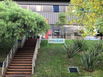 Vista exterior de la sede de Satellogic. Una escalera de madera con barandillas metálicas sube a un edificio moderno gris. Un letrero de Satellogic se encuentra en un césped verde