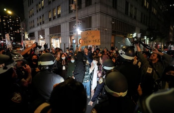 Manifestantes con mascarillas y agentes de policía con cascos en una calle de Nueva York de noche; un hombre sostiene un cartel que dice 'ICE OUT OF NEW YORK' frente a un edificio