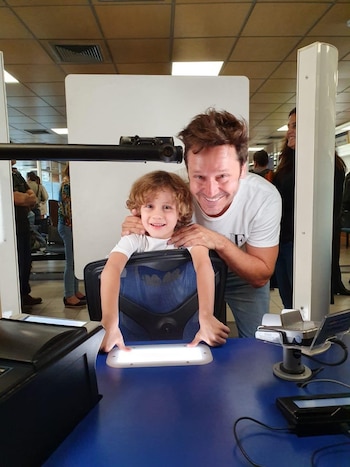Benjamín Vicuña sostiene por los hombros a su hijo Benicio, quien apoya sus dedos sobre un lector iluminado en una mesa azul