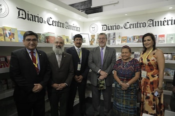 Seis personas, cuatro hombres y dos mujeres, posan de pie frente a una pared con el logo y el nombre de Diario de Centro América, flanqueados por estanterías con libros