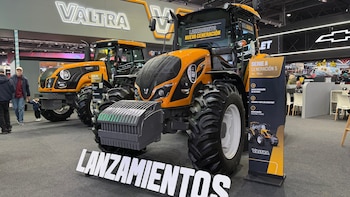 Dos tractores Valtra naranja y negro en una sala de exposición. Señales con texto "VALTRA", "LANZAMIENTO NUEVA GENERACIÓN" y "LANZAMIENTOS". Personas en el fondo