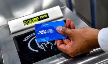 Una mano sostiene una tarjeta azul de la Autoridad de Transporte Urbano. Un lector metálico muestra en su pantalla la fecha y el estado "BLOQUEADO"