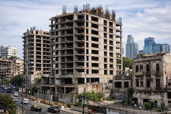 Vista aérea de varios edificios de hormigón abandonados y en construcción en una zona urbana con tráfico vehicular y graffiti. Al fondo, rascacielos modernos.