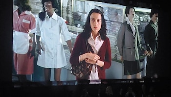 Una mujer con cárdigan granate, camisa blanca y bolso marrón está de pie entre cuatro maniquíes con diferentes uniformes de trabajo