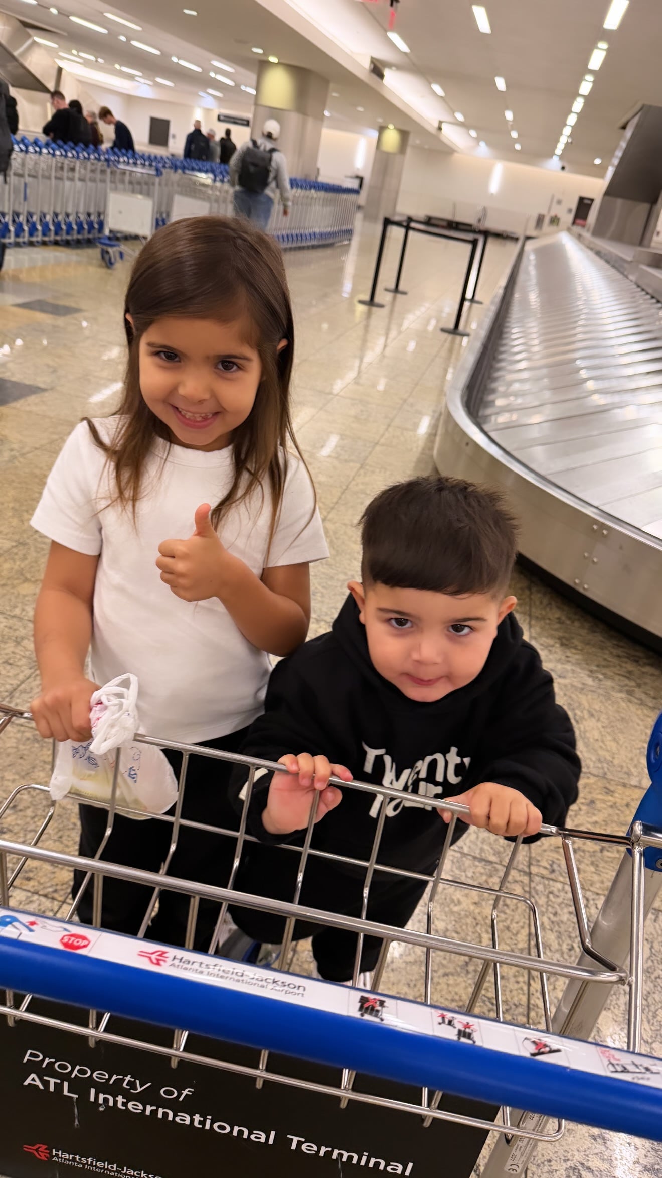 Olivia y Benjamín, los hijos de Valentina Cervantes y Enzo Fernández, posan sonrientes en el aeropuerto de Hartsfield-Jackson antes de su viaje a Estados Unidos para reunirse con su padre.