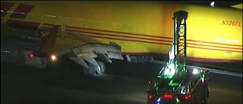 Un avión de carga amarillo junto a un camión de bomberos iluminado con luces de emergencia en una pista nocturna