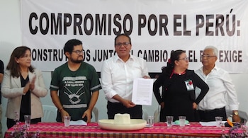 Grupo de cinco personas de pie detrás de una mesa con mantel, frente a un banner blanco con texto político. El hombre central de camisa blanca sostiene un documento.