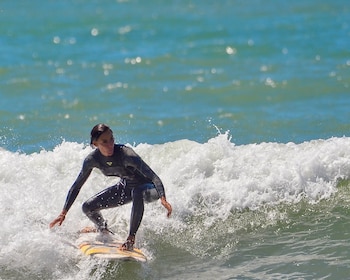 Una mujer con traje de neopreno negro se desplaza sobre una tabla de surf en medio de la espuma de una ola