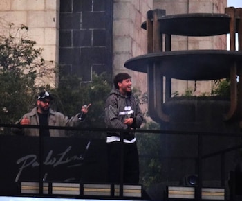 Dos hombres sobre una plataforma con la firma de Paulo Londra, uno con sudadera a rayas y otro con gorra y micrófono