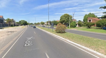 Una carretera de asfalto con vehículos en movimiento, un cantero central con vegetación y árboles en los márgenes