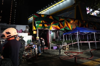 Vista nocturna del exterior de un local con fachada colorida. Personal de emergencia, una camilla, mangueras rojas y cinta de seguridad en la acera