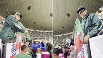 Hombre con gorra, gafas y chaqueta verde sujetando bandera de México en un estadio; se observa a la multitud y un techo abovedado con objetos colgantes