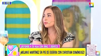 Melanie Martínez, mujer de cabello castaño claro, sentada en un set de televisión con blusa estampada, micrófono y fondo de pantallas coloridas