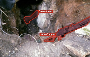 Agujero en la tierra con un cuerpo parcialmente visible y un arma resaltados en rojo. El suelo y las rocas rodean la escena