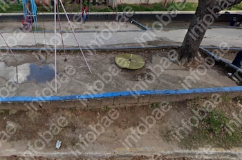 Vista aérea de un parque infantil con columpios, charcos de agua en el suelo de tierra y cemento, un juego giratorio, y un árbol