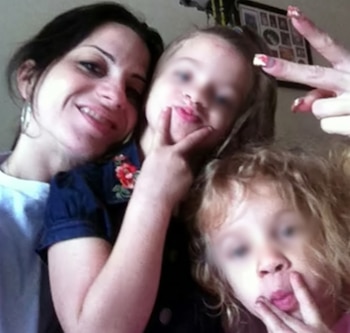 Una mujer sonriente posa junto a dos niñas pequeñas que hacen gestos con los dedos frente a la cámara