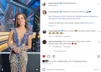 Suheyn Cipriani posa sonriente en un escenario con un vestido azul y plateado con pedrería, mangas largas transparentes y un pronunciado escote en V